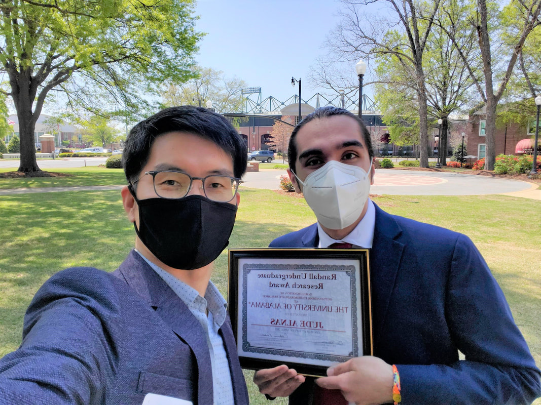 two men with masks on in suits outside holding a framed award